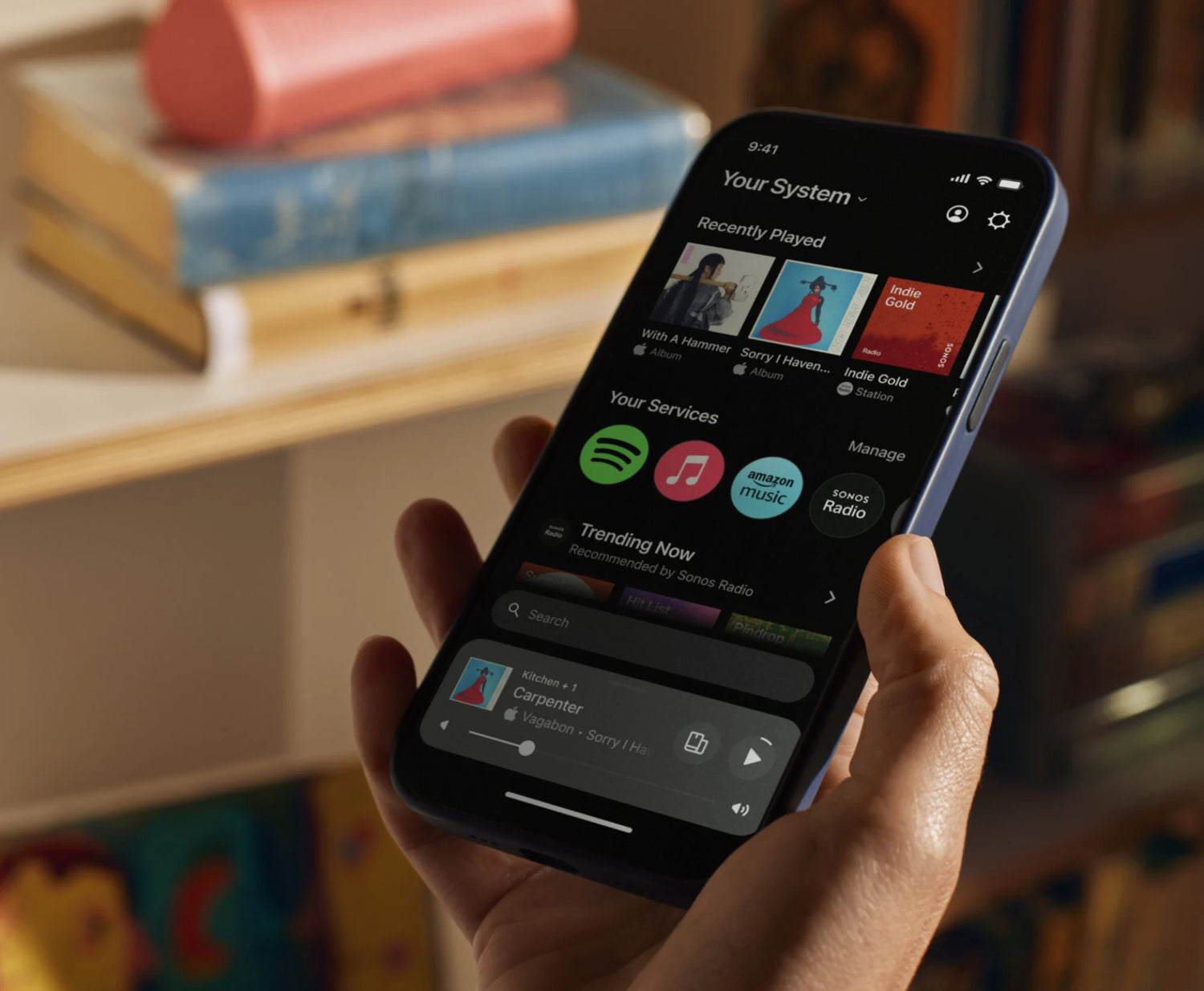 Person holding a smartphone displaying the Sonos app interface, ready to play music